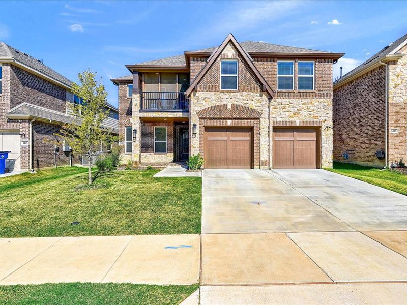 View of front facade featuring a front yard, a balcony, and a garage