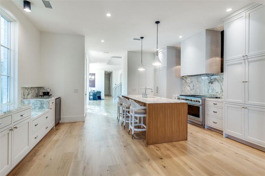 Kitchen featuring light stone counters, stainless steel range, an island with sink, and white cabinetry