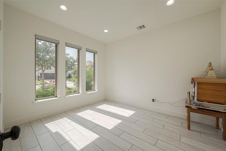 This is a bright, airy room with large windows allowing for plenty of natural light, complemented by recessed lighting. It features a clean, neutral color palette and modern tile flooring, offering a versatile space ready for personalization.