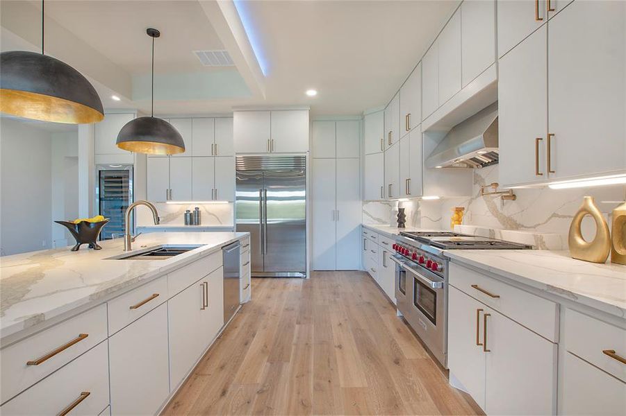 Kitchen with light hardwood / wood-style flooring, decorative backsplash, pendant lighting, high quality appliances, and sink