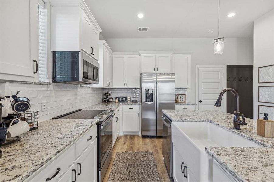 Kitchen with appliances with stainless steel finishes, decorative backsplash, pendant lighting, and light wood-type flooring