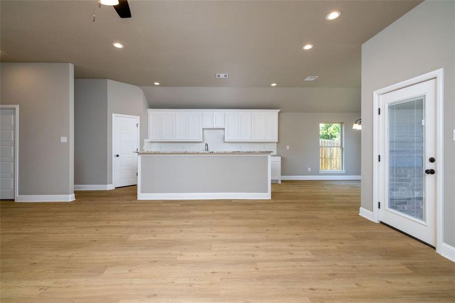 Kitchen with white cabinets, a center island with sink, light hardwood / wood-style floors, light stone countertops, and ceiling fan