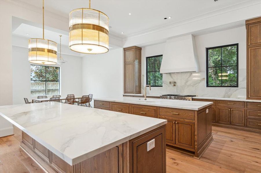 This chef's kitchen is a masterpiece, featuring SubZero and Wolf appliances, stunning stained white oak cabinetry, and Ralph Lauren brass pendants for a touch of elegance. Dual islands with Dekton quartz countertops offer ample space for meal prep and breakfast bar seating, combining style with practicality.