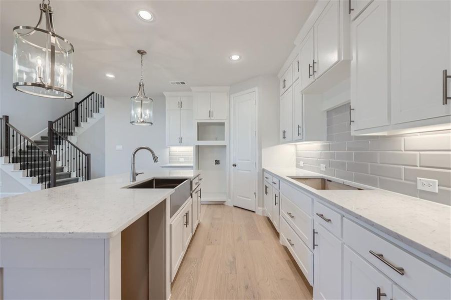 Kitchen featuring light hardwood / wood-style flooring, tasteful backsplash, light stone counters, decorative light fixtures, and a center island with sink