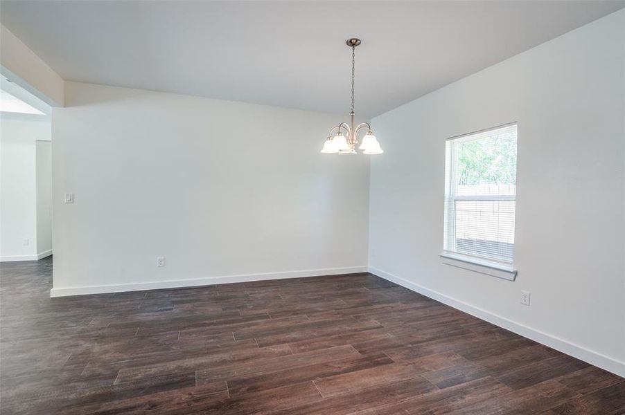 Empty room featuring a notable chandelier and dark wood-type flooring