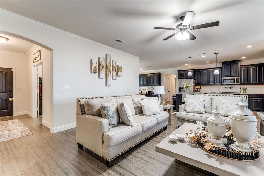 Living room with wood-type flooring, ornamental molding, and ceiling fan