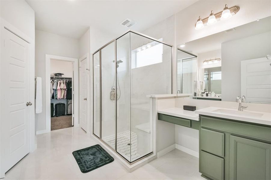 This is a bright, modern bathroom featuring a dual-sink vanity with dark green cabinets, a large mirror, a glass-enclosed shower.