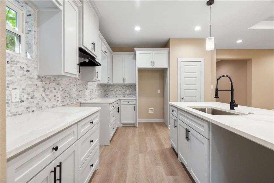 Kitchen with sink, light stone countertops, pendant lighting, light wood-type flooring, and white cabinetry