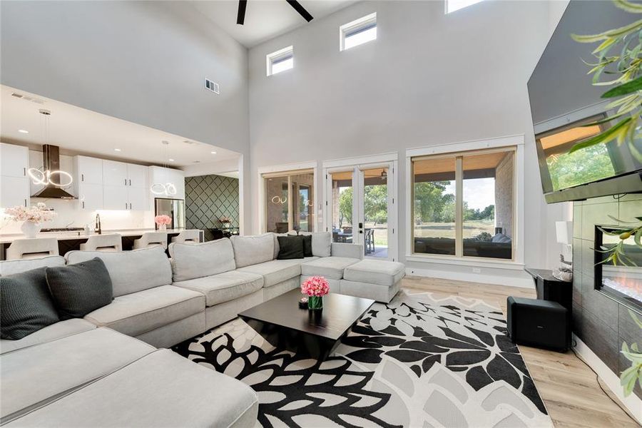 Living room featuring a high ceiling, a tiled fireplace, ceiling fan, and light wood-type flooring