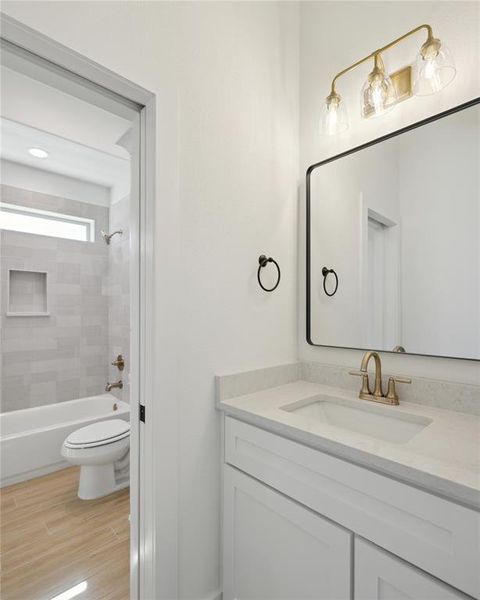 Full bathroom featuring hardwood / wood-style floors, tiled shower / bath, toilet, and vanity