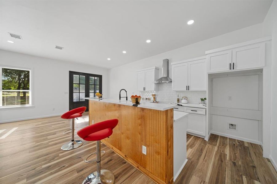 Kitchen featuring light hardwood / wood-style flooring, tasteful backsplash, a center island with sink, and wall chimney range hood