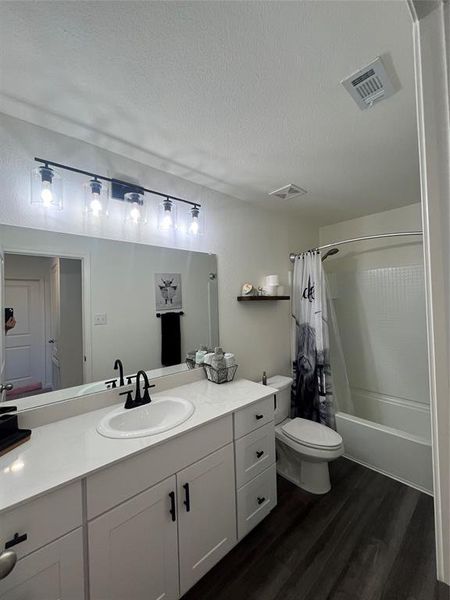 Full bathroom with a textured ceiling, hardwood / wood-style floors, toilet, vanity, and shower / tub combo with curtain