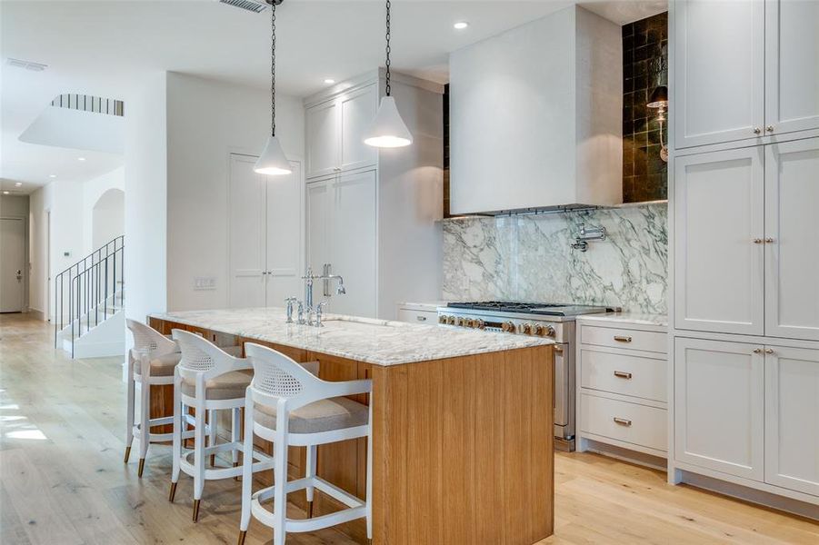 Kitchen featuring white cabinets, hanging light fixtures, stainless steel stove, light wood-type flooring, and a center island with sink