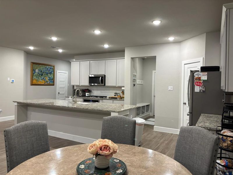 This is a modern, open-plan kitchen with white cabinetry, granite countertops, stainless steel appliances, and recessed lighting. A breakfast bar and an adjacent dining area offer ample space for meals and entertaining.