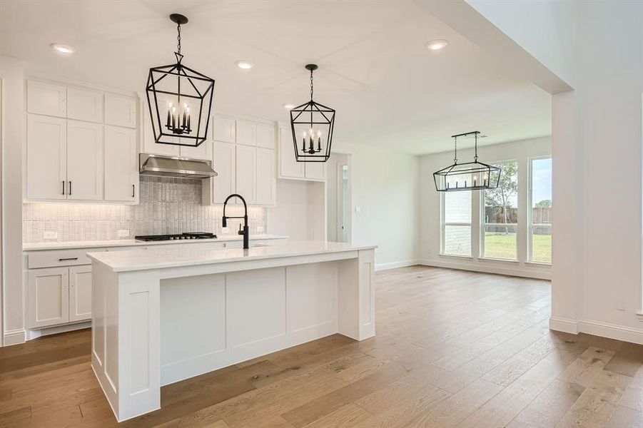 Kitchen with decorative light fixtures, white cabinetry, decorative backsplash, light hardwood / wood-style floors, and a kitchen island with sink