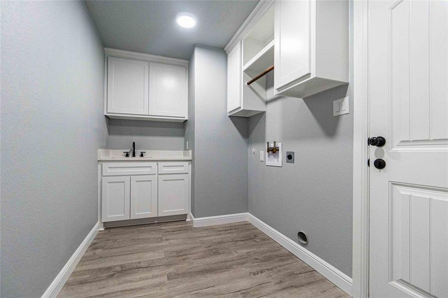 Clothes washing area with electric dryer hookup, cabinets, sink, and light hardwood / wood-style flooring