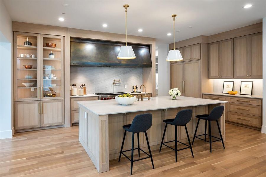 Kitchen featuring range hood, a kitchen island with sink, a kitchen bar, and light hardwood / wood-style flooring