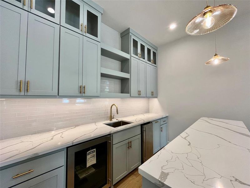 Kitchen with pendant lighting, beverage cooler, backsplash, and light stone counters