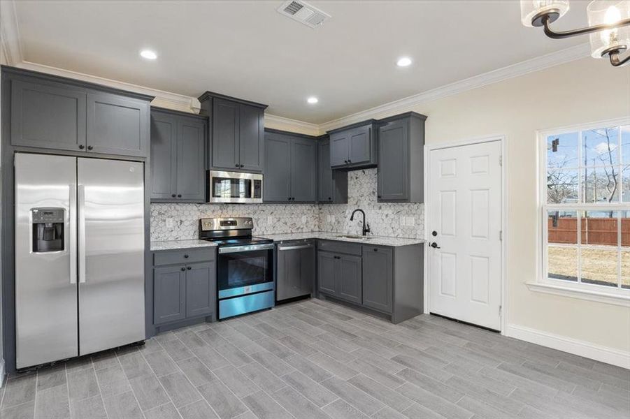 Kitchen with stainless steel appliances, sink, backsplash, and a healthy amount of sunlight