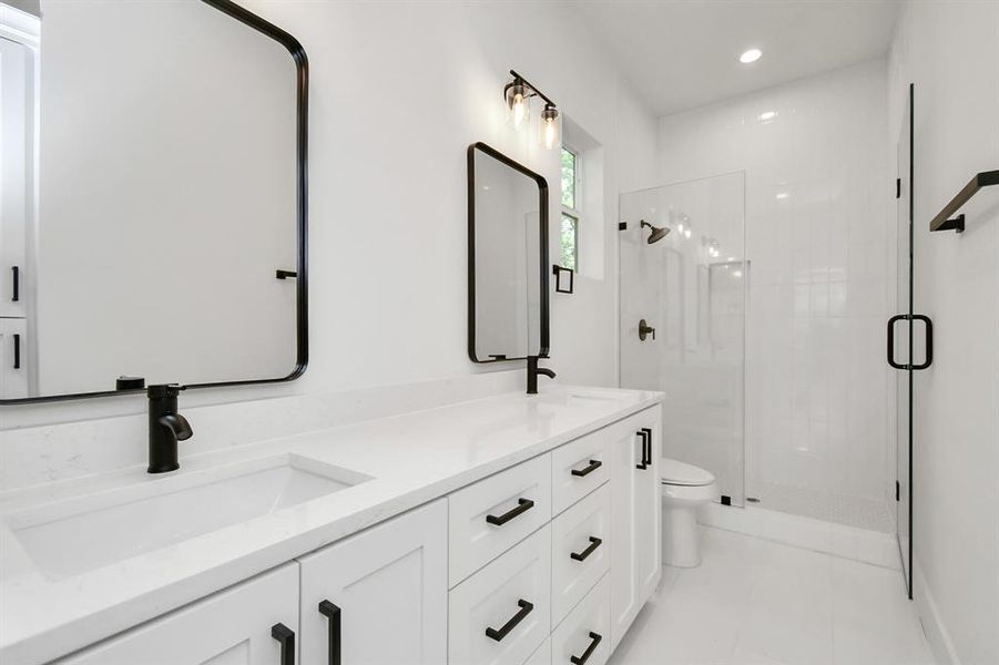 The primary bathroom shines with dual sinks, plenty of storage, and sleek mirrors. Two vanity lights brighten the space, which includes a walk-in shower with oversized subway tiles.