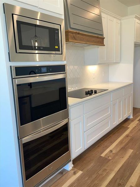 Kitchen with hardwood / wood-style floors, tasteful backsplash, custom exhaust hood, stainless steel appliances, and white cabinetry