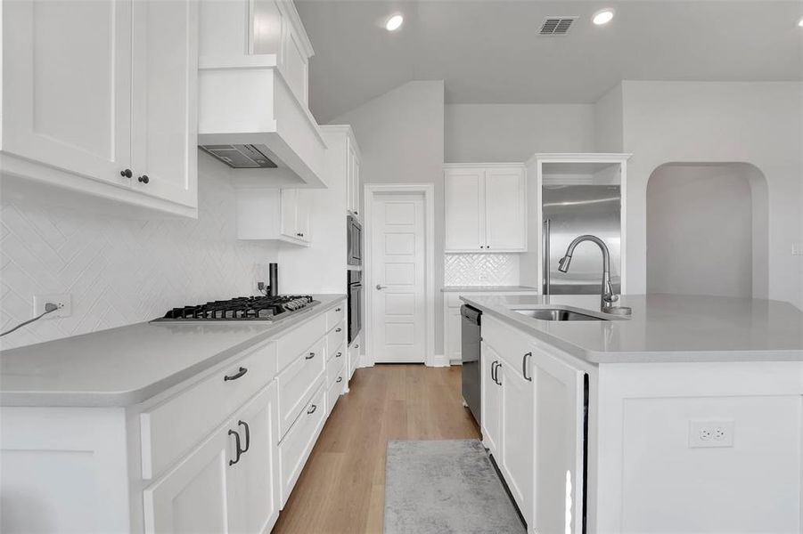 Kitchen with white cabinets, an island with sink, appliances with stainless steel finishes, and light hardwood / wood-style floors