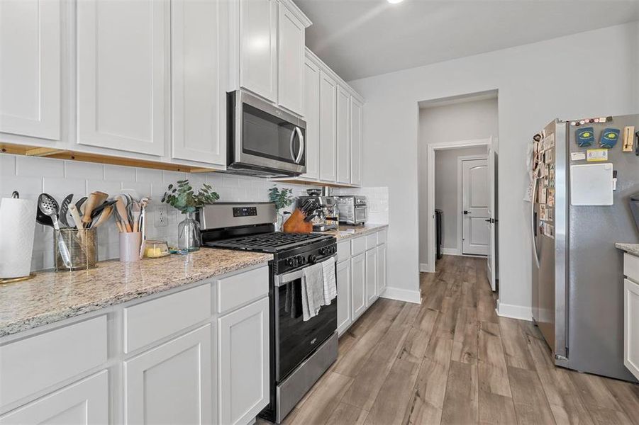 Kitchen featuring white cabinets, light stone counters, backsplash, light hardwood / wood-style flooring, and stainless steel appliances