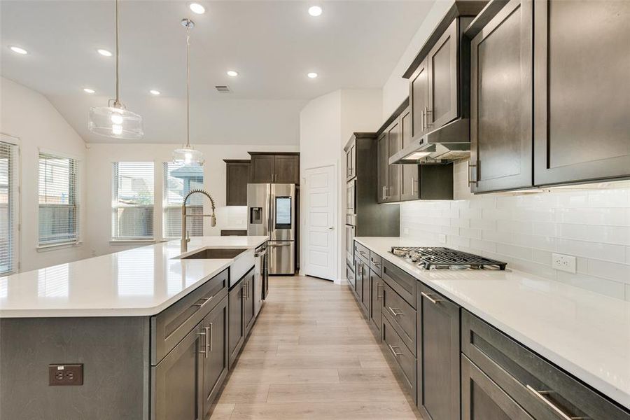 Kitchen with appliances with stainless steel finishes, light hardwood / wood-style floors, sink, lofted ceiling, and an island with sink