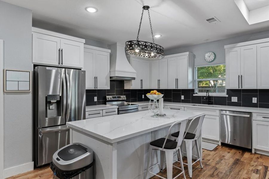 Kitchen featuring sink, a kitchen island, light hardwood / wood-style flooring, appliances with stainless steel finishes, and premium range hood