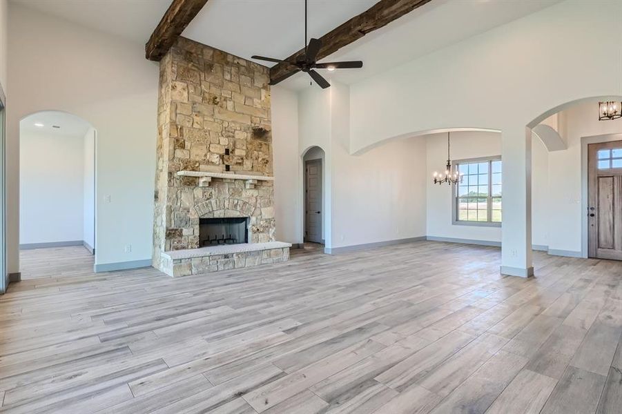 Unfurnished living room with a fireplace, beamed ceiling, light wood-type flooring, and ceiling fan with notable chandelier