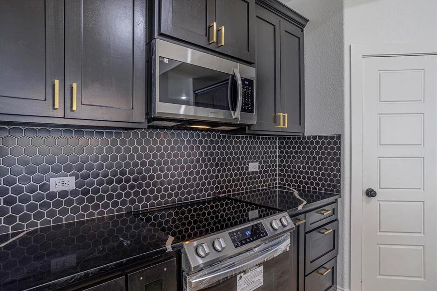 Kitchen with backsplash, dark stone countertops, and appliances with stainless steel finishes