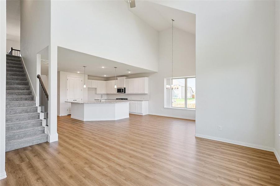 Unfurnished living room with light hardwood / wood-style floors, an inviting chandelier, sink, and high vaulted ceiling