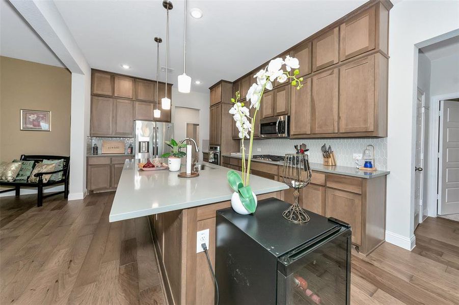 Kitchen featuring wine cooler, tasteful backsplash, appliances with stainless steel finishes, a kitchen island with sink, and light hardwood / wood-style flooring