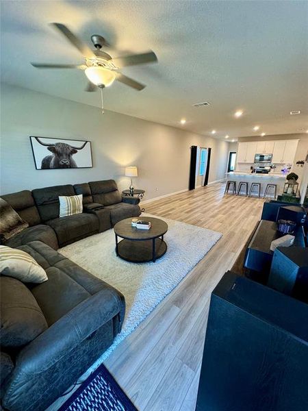 Living room with light wood-type flooring, ceiling fan, and a textured ceiling