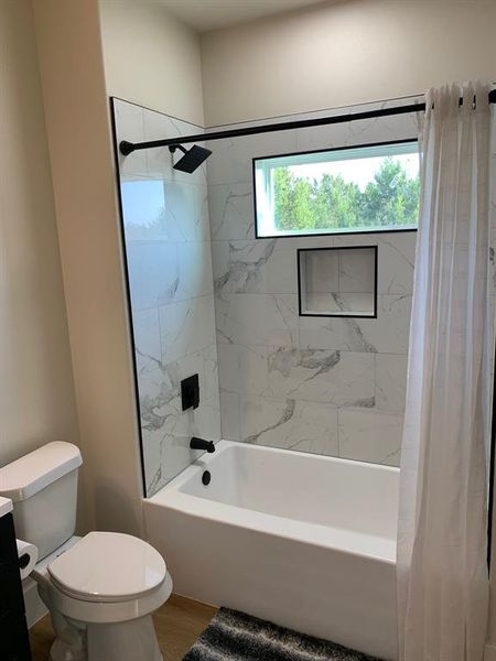 Bathroom with toilet, shower / bath combo with shower curtain, and wood-type flooring