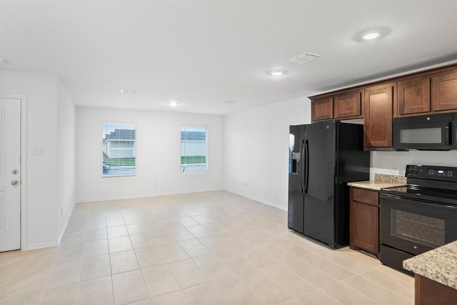 Kitchen with dark brown cabinetry, light stone countertops, light tile patterned floors, and black appliances