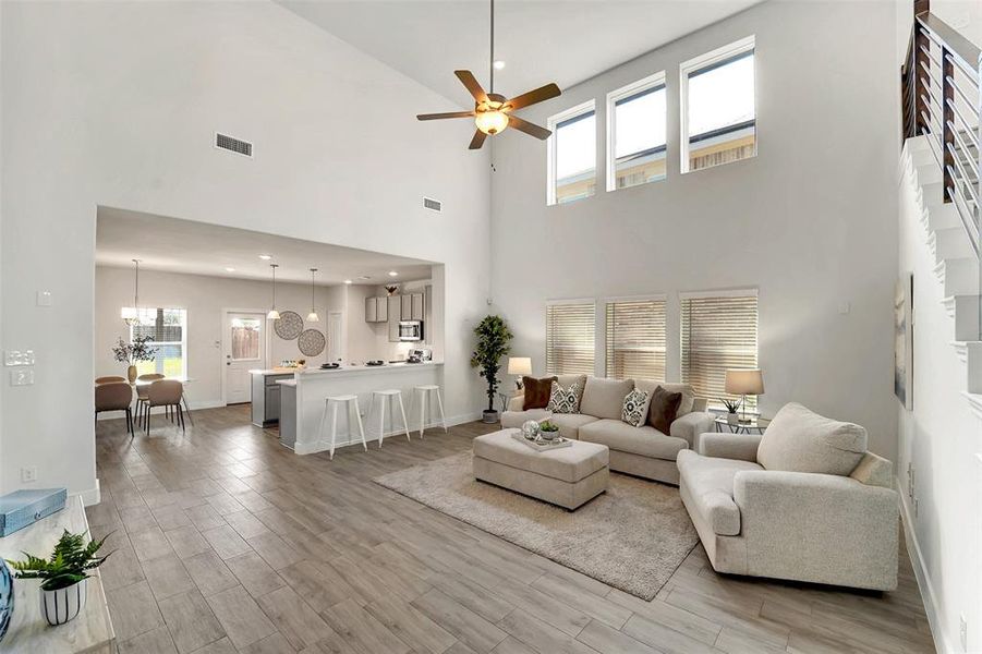 Living room featuring a high ceiling, plenty of natural light, ceiling fan with notable chandelier, and light hardwood / wood-style flooring