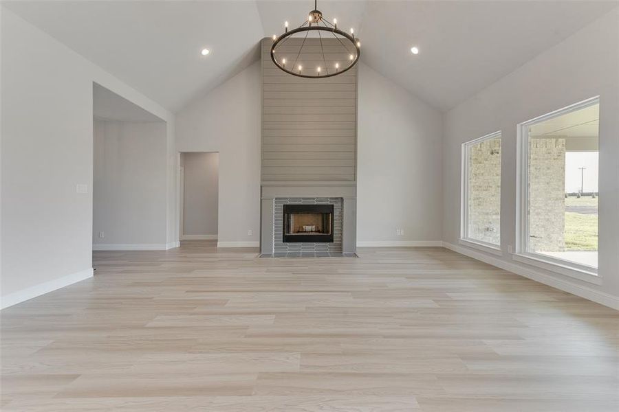 Unfurnished living room featuring a chandelier, light hardwood / wood-style floors, high vaulted ceiling, and a tile fireplace