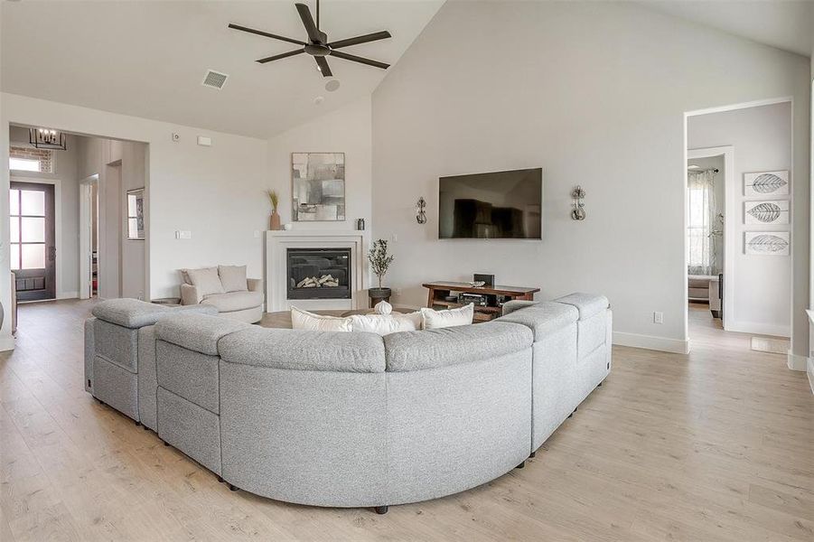 Living room featuring ceiling fan, high vaulted ceiling, and light hardwood / wood-style flooring