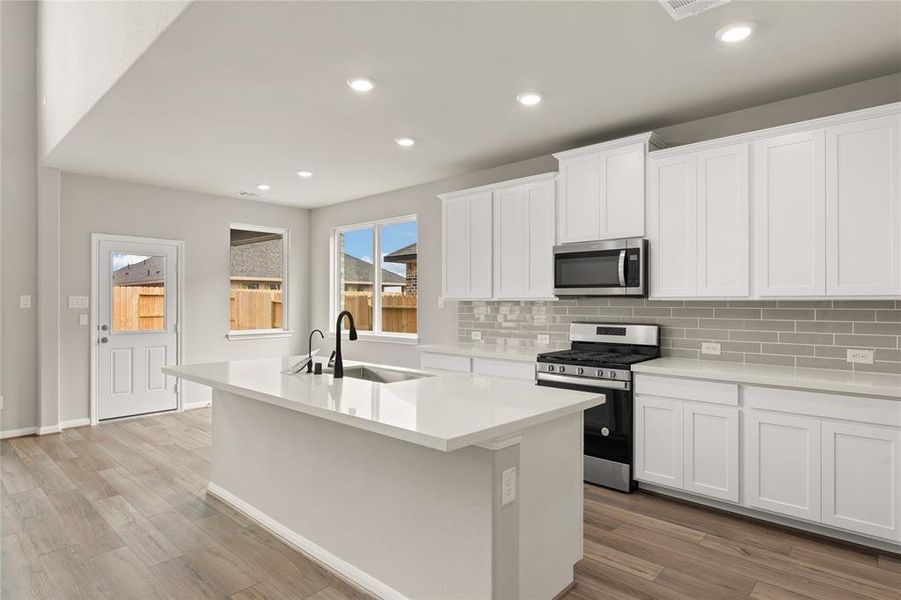This light and bright kitchen features a large quartz island, white cabinets, a large sink overlooking your family room, recessed lighting, and beautiful backsplash.