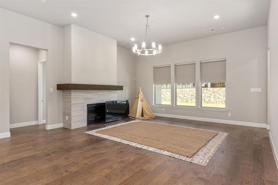 Unfurnished living room featuring a tiled fireplace, a chandelier, and dark hardwood / wood-style flooring