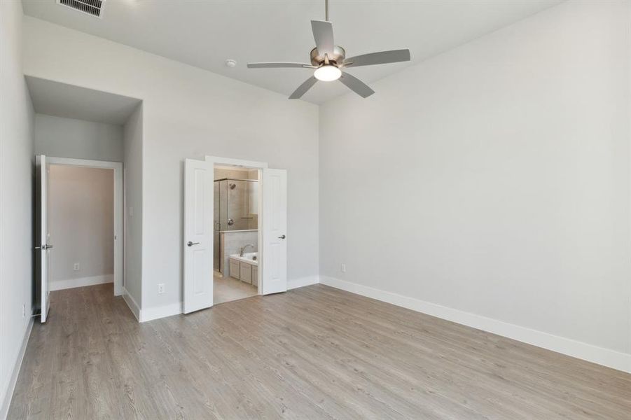 Unfurnished bedroom featuring light wood-type flooring, ensuite bathroom, and ceiling fan