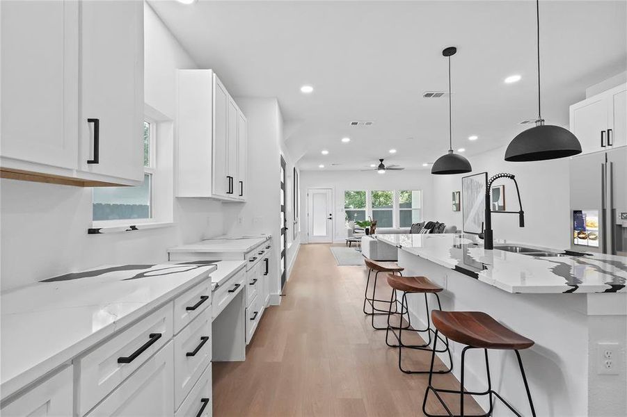 Kitchen with a breakfast bar area, light wood-type flooring, white cabinets, light stone counters, and an island with sink