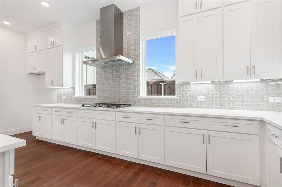 Kitchen with white cabinets, dark hardwood / wood-style floors, backsplash, and wall chimney exhaust hood
