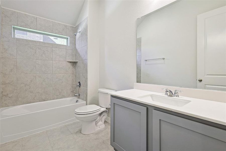 Full bathroom with vaulted ceiling, vanity, tiled shower / bath combo, toilet, and tile patterned floors