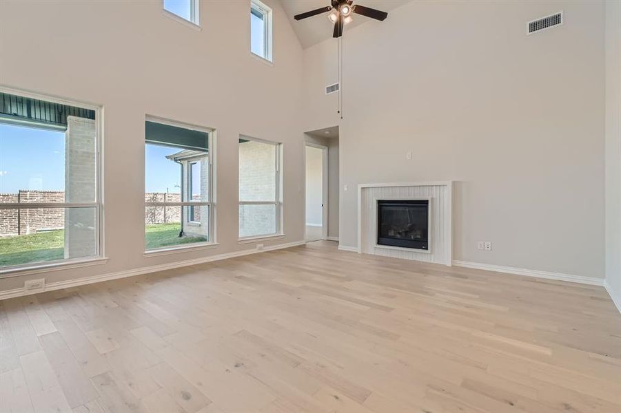 Unfurnished living room with high vaulted ceiling, light wood-type flooring, and ceiling fan