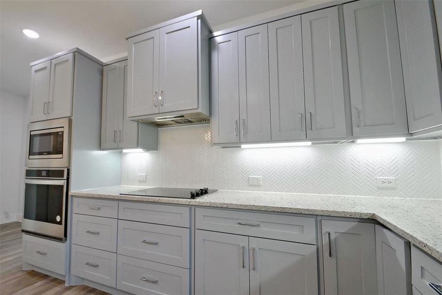 Kitchen with light stone counters, tasteful backsplash, gray cabinets, appliances with stainless steel finishes, and light wood-type flooring