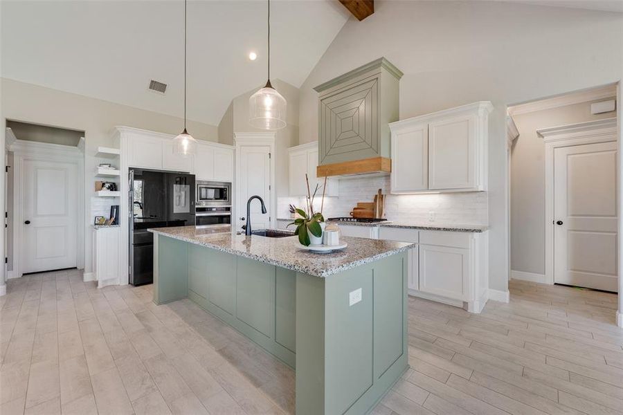 Kitchen with appliances with stainless steel finishes, hanging light fixtures, high vaulted ceiling, and white cabinetry