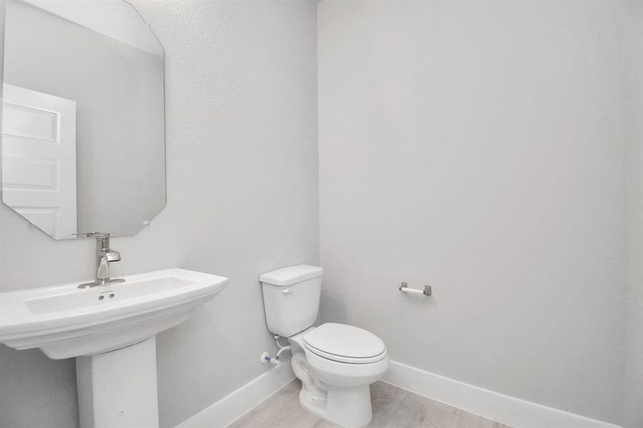 Experience modern elegance in this charming half bathroom, boasting a sophisticated 5-panel door, upgraded pedestal sink, contemporary hardware, and stylish vanity lights. The warm paint palette bathes the area in a welcoming glow, creating a bright and inviting atmosphere.