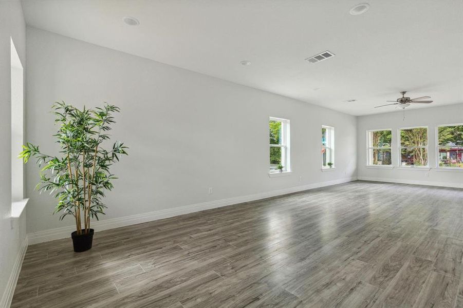 Empty room featuring dark wood-type flooring, ceiling fan, and a healthy amount of sunlight